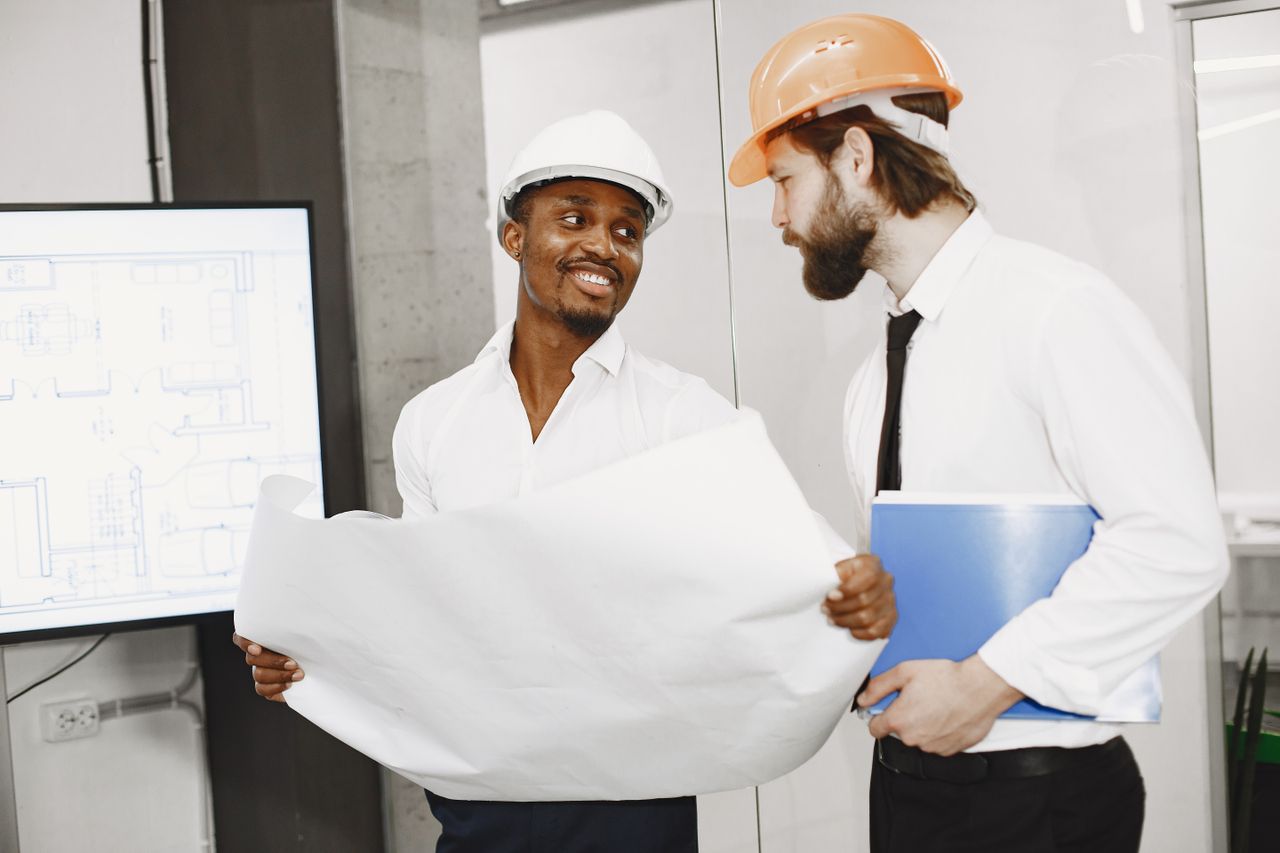 The Art of Drawing Readers In: Your attractive post title goes here Two architects in hard hats discuss blueprints in a modern office setting, highlighting teamwork and planning.